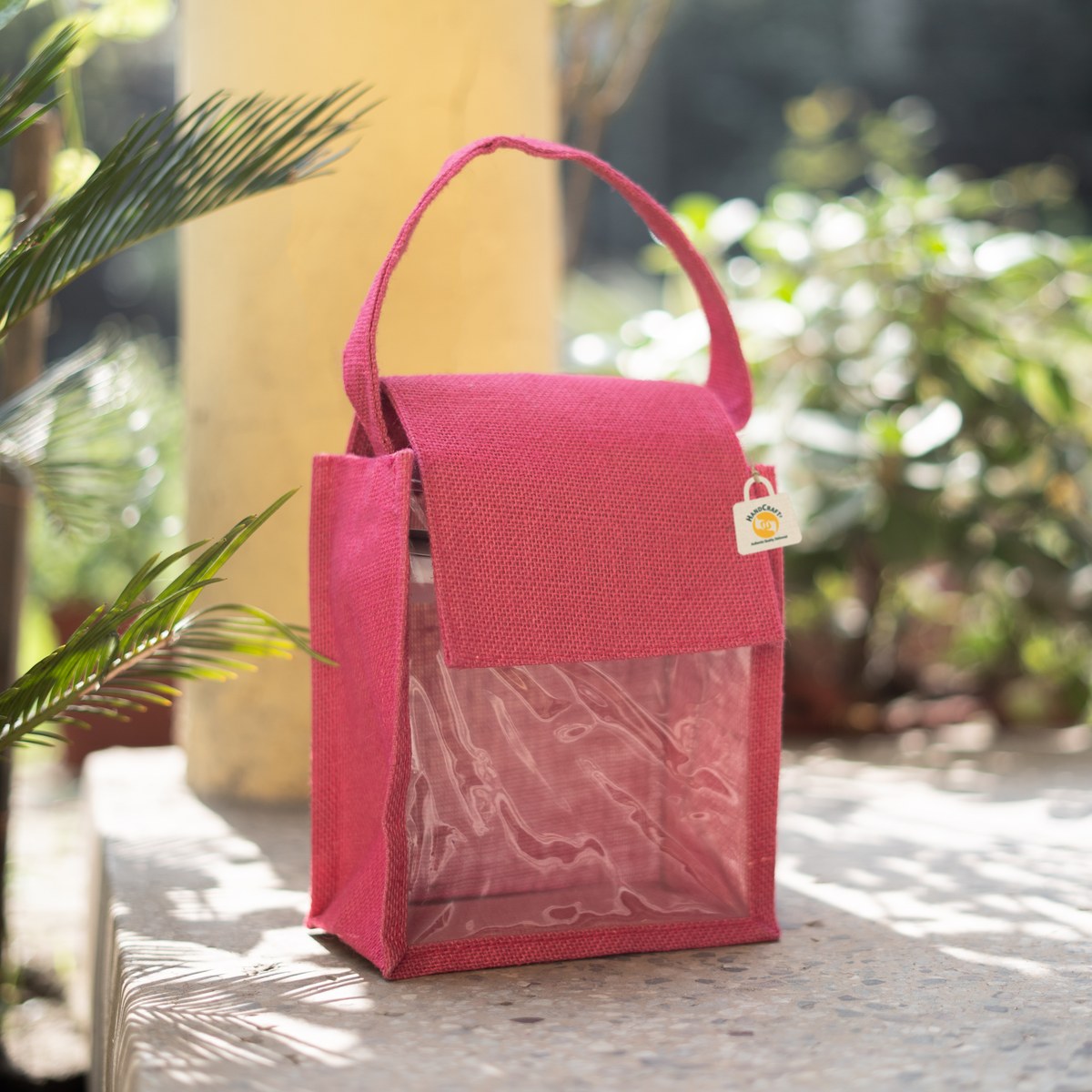 Pink jute gift bag with a clear front window, a top flap and a single handle.